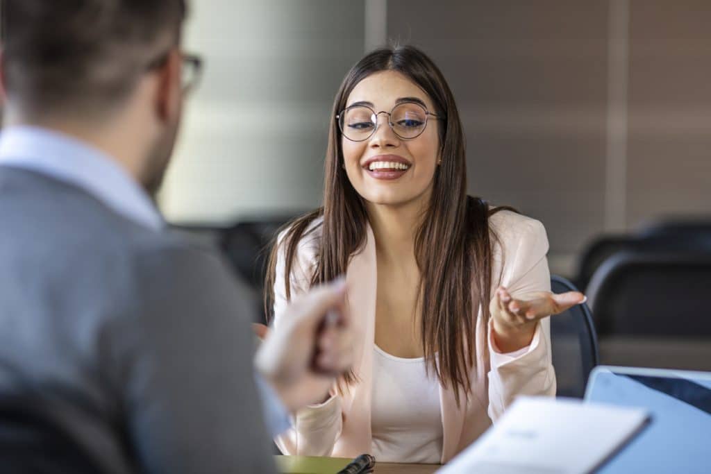 Applicant smiling and holding resume while sitting in front of HR manager during job interview